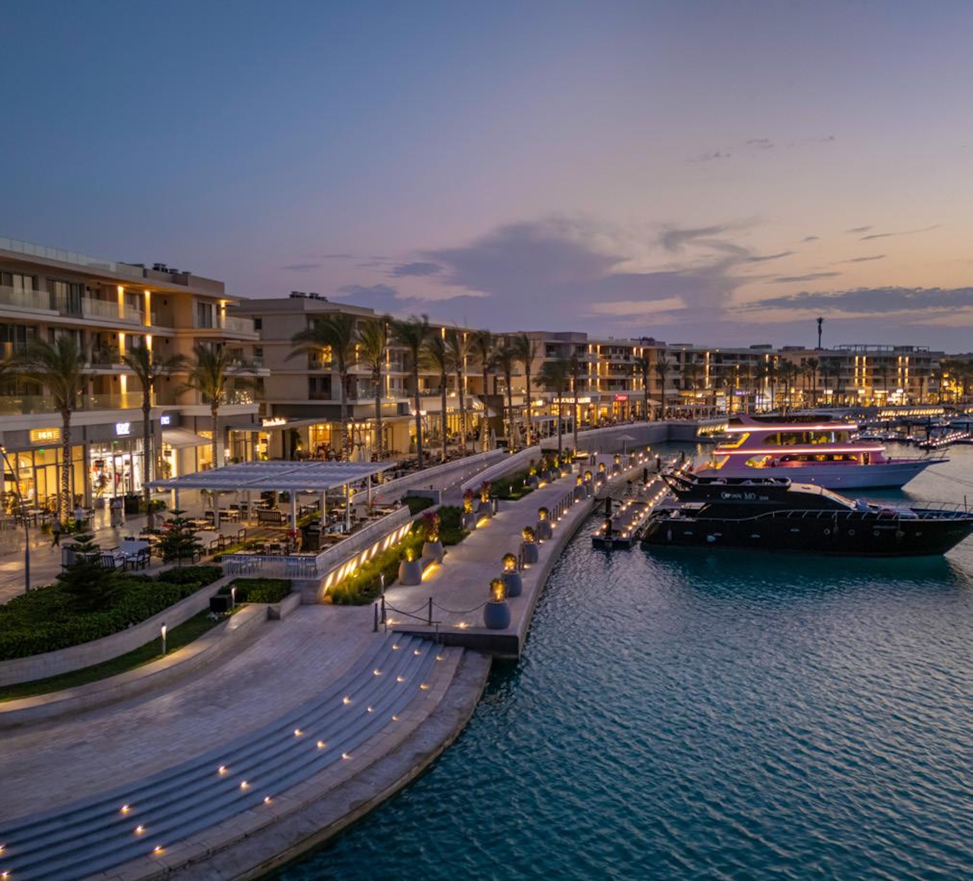 ممشى الواجهة المائية في مارينا مراسي وقت الغروب مع مطاعم ومحلات ويخوت راسية